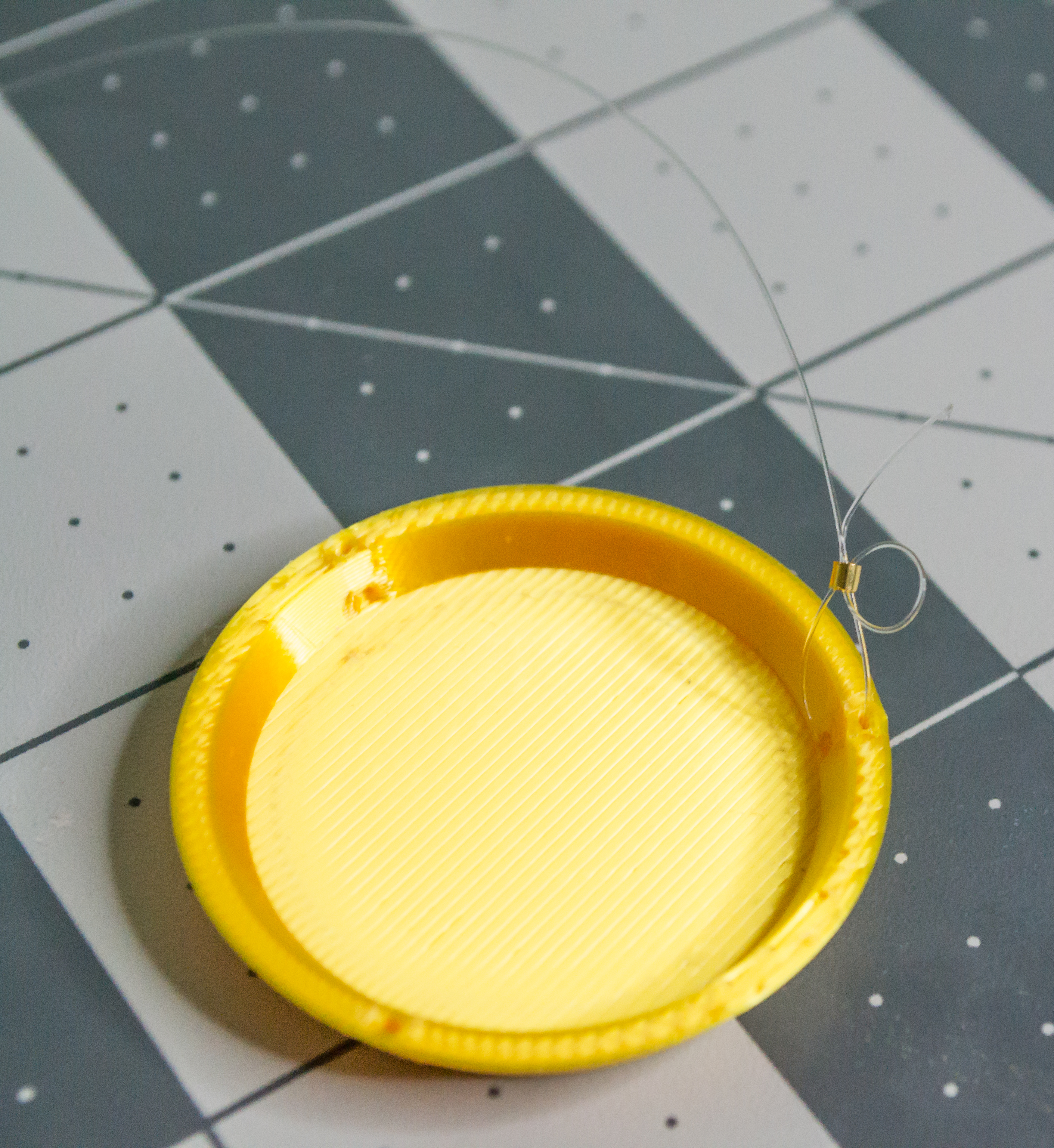 A small gold crimp bead on the monofilament of a 3D printed gold plate. There is a loop around the gold crimp bead and the line goes both ways through it.
