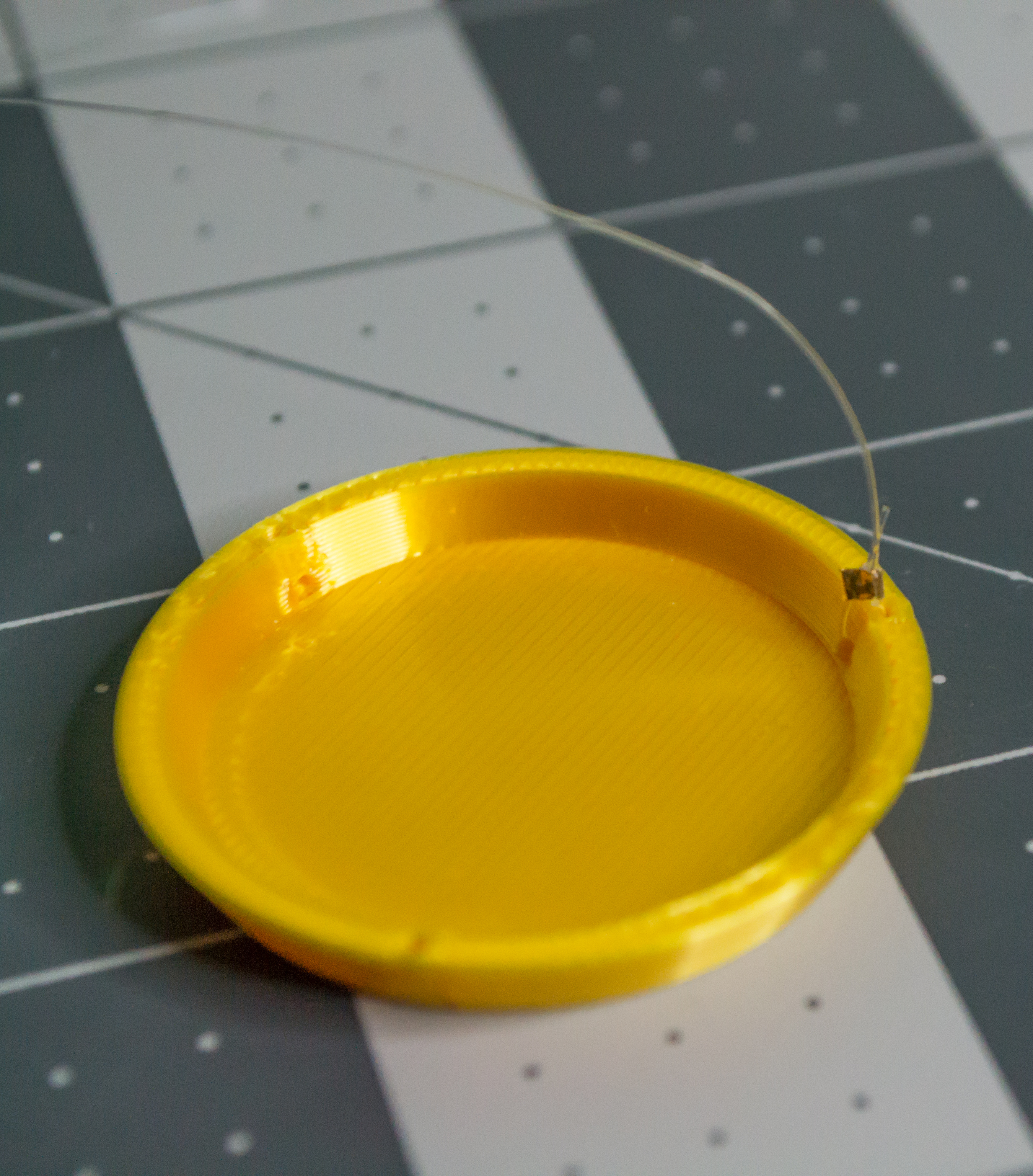 Crimped small gold bead to hold gold 3D printed plate on monofilament.