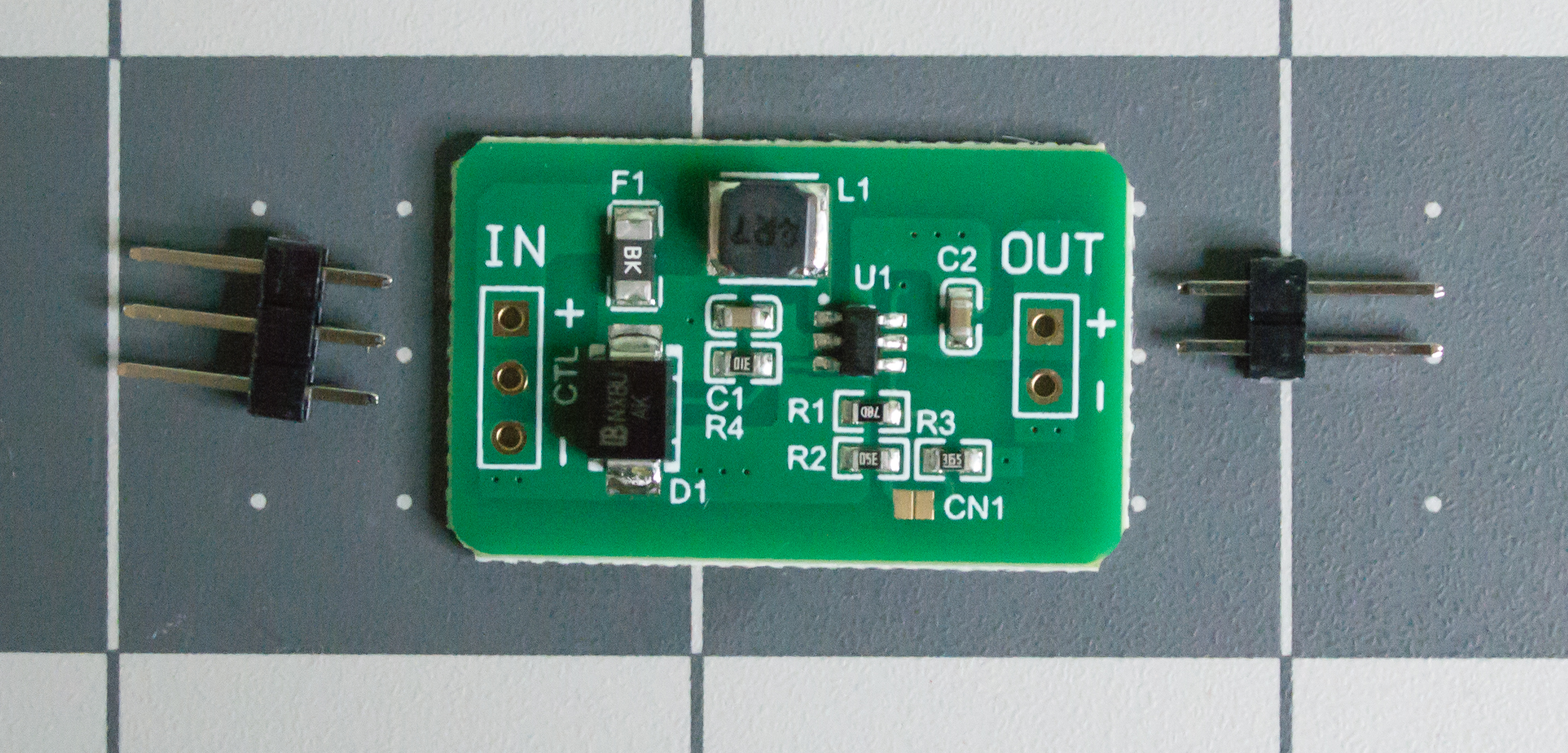 QEBIDUM DC-DC converter board with the necessary header pins lying next to it.